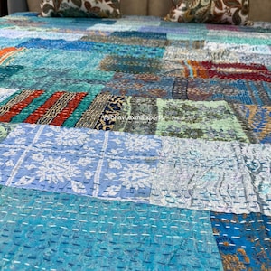 May include: A patchwork quilt in shades of blue, teal, and orange, with a variety of patterned fabric squares. The quilt is adorned with decorative stitching and features a mix of floral and geometric designs. Two decorative pillows with floral patterns are visible in the background.