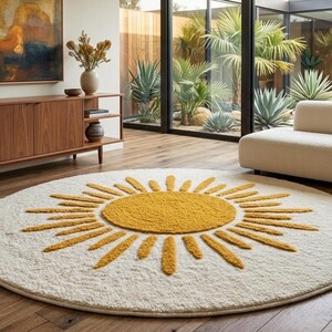 May include: A round, cream-colored rug with a large yellow sun design in the center. The rug is placed on a hardwood floor in a living room setting. The room also features a mid-century modern style wooden cabinet and a cream-colored sofa.