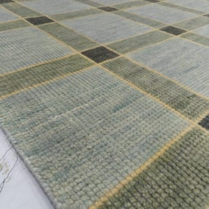 May include: A rectangular area rug with a geometric pattern. The rug features a grid design with squares and rectangles in shades of blue, green, and black. Yellow lines separate the shapes. The rug has a textured surface.