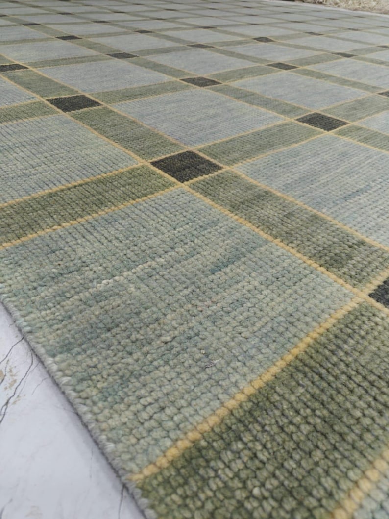 May include: A rectangular area rug with a geometric pattern. The rug features a grid design with squares and rectangles in shades of blue, green, and black. Yellow lines separate the shapes. The rug has a textured surface.
