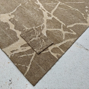 May include: A brown and beige area rug with a matching small rug. The rug has a textured surface and a pattern of beige, vein-like lines across the brown background. The rug is made of a woven material.