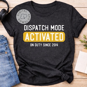 Pode incluir: T-shirt cinzenta escura com o texto "DISPATCH MODE ACTIVATED" em branco e amarelo, com "ON DUTY SINCE 2014" abaixo. A camisa é exibida com jeans azuis e fones de ouvido pretos.