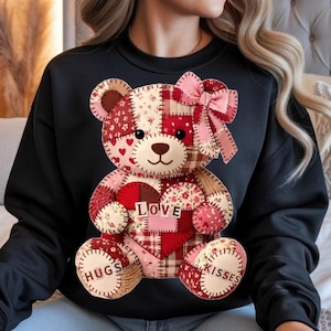 Könnte beinhalten: Schwarzes Sweatshirt mit einem Patchwork-Teddybär-Design. Der Bär hat ein Herz mit dem Wort "LOVE" und den Worten "HUGS" und "KISSES" auf seinen Pfoten. Der Bär besteht aus verschiedenen Stoffen in Rot-, Rosa- und Beigetönen.