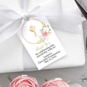 May include: A white thank you tag with gold and pink floral accents. The tag features a gold circle with a chalice and host inside. The text reads "Thank You for celebrating this special day with us! Lauren's First Holy Communion May 12, 2022".