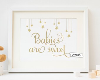 May include: A white frame with a gold print that reads "Babies are sweet" with gold stars hanging from the top. The print is on a white background and has a small white tag that says "printable".