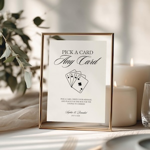 May include: A rectangular gold-toned metal frame holding a white card with black text that reads PICK A CARD Any Card, followed by instructions to write a message for the couple, and the names Sophie & Benedict with the date JULY 23 2028.