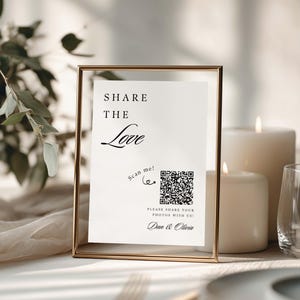 May include: A rectangular gold metal frame holding a white sign with black text that reads SHARE THE LOVE, scan me! with a heart icon, a QR code, PLEASE SHARE YOUR PHOTOS WITH US!, and the names Dan & Olivia in a script font.