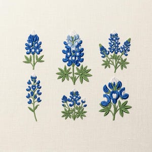 May include: Embroidered bluebonnet flowers in various stages of bloom, with green leaves and white accents, are displayed on a cream-colored fabric. The floral designs are detailed and arranged in a visually appealing composition.