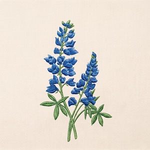 May include: Embroidered image of two bluebonnet flower stalks with green leaves. The blue flowers are in full bloom, with detailed stitching. The background is a light beige fabric, providing a neutral backdrop for the vibrant floral design.