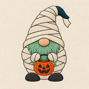 Op de afbeelding: Een geborduurde kabouterfiguur gewikkeld in gebroken witte windsels als een mummie, met een lichtgroene baard, een beige neus en donkergrijze schoenen. De kabouter houdt een kleine oranje pompoenemmer vast met een zwart gezicht.