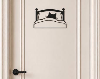 May include: A black metal wall decoration featuring a silhouette of a cat tucked into a bed with a pillow and blanket. The cat's head and ears are visible above the covers, while the bed frame includes a headboard with two posts.