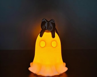 May include: A glowing orange ghost-shaped lamp with a solid black cat figurine perched on top. The ghost figure features two circular cutouts for eyes and a scalloped base, emitting a warm, bright light from within its translucent structure.