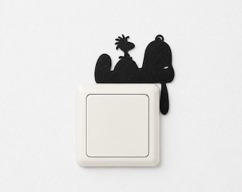 May include: A matte black decorative wall decal featuring the silhouette of a cartoon dog and a small bird perched on its head, positioned directly above a square white light switch with a smooth, clean finish and a simple rocker mechanism.