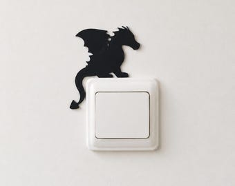 May include: A black dragon silhouette decal positioned above a square white light switch. The dragon is depicted in profile with wings spread, a long tail, and spikes along its back, appearing to perch on the top edge of the light switch plate.
