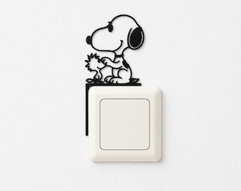 May include: A black metal wall decal featuring the cartoon character Snoopy and Woodstock sitting on top of a white square light switch. The design is a thin, flat silhouette that attaches to the corner of the light switch plate on the wall.
