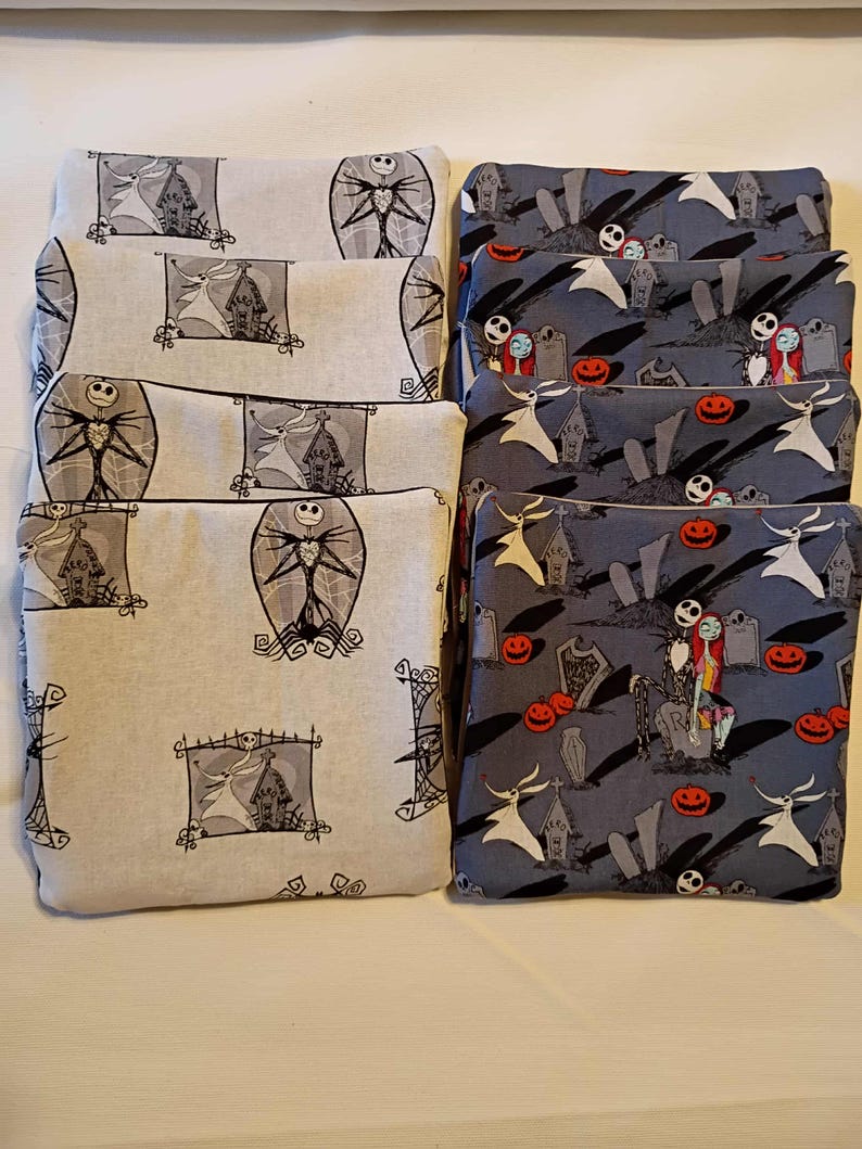 May include: A collection of rectangular fabric pouches. Some pouches are light gray with black and white illustrations of a tall, thin figure and a haunted house. Other pouches are dark gray with Halloween-themed illustrations.