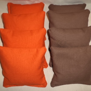 May include: Set of 8 bean bags, 4 orange and 4 brown. The bean bags are made of a soft, textured fabric.
