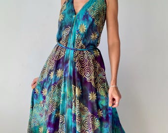 Può includere: Un lungo abito all'americana fluido nei toni del verde acqua, viola e oro. L'abito presenta una vita annodata ed è decorato con motivi a spirale e a stella dorati. Il tessuto ha un effetto tie-dye, creando un look unico e artistico.