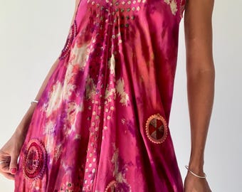 Può includere: Un vivace abito rosa con scollo all'americana e scollatura a V. L'abito presenta un motivo tie-dye con accenti bianchi e viola e decorazioni circolari. L'abito è realizzato in un tessuto fluido.