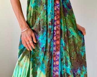 May include: A flowing, sleeveless dress in shades of green, teal, and purple, adorned with a delicate floral pattern. The dress features a central panel with intricate floral embroidery in orange, purple, and blue. The fabric appears lightweight and suitable for warm weather.