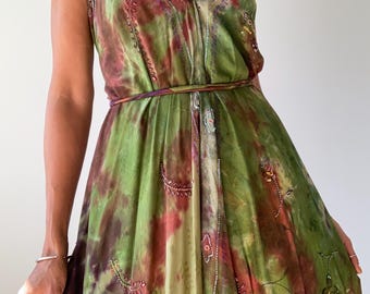 May include: A flowing, tie-dye maxi dress in shades of green, burgundy, and cream. The dress features a halter neckline, a cinched waist, and delicate embroidered details. The dress is a bohemian style.
