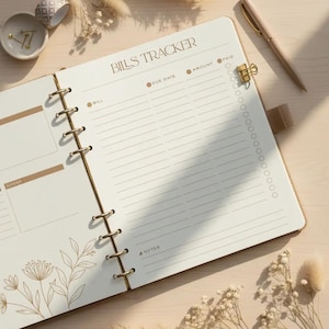 Pode incluir: Um planejador Bills Tracker creme com detalhes dourados. O planejador apresenta uma encadernação em espiral dourada, uma caneta e um clip dourado. As palavras "BILLS TRACKER" são impressas no topo. Flores secas e uma pequena tigela com design dourado também são visíveis.