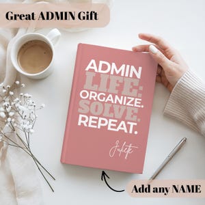 May include: A pink journal with the text "ADMIN LIFE: ORGANIZE. SOLVE. REPEAT." in white and taupe lettering. The journal has a personalized name and the words "Add any NAME" are also visible. A cup of coffee and a pen are also in the image.