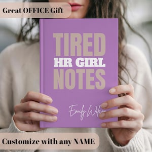 Könnte beinhalten: Ein lila Notizbuch mit dem Text "TIRED HR GIRL NOTES" in Beige und Weiß. Der Name "Emily Wilson" ist kursiv geschrieben. Das Notizbuch wird von einer Person gehalten. Der Text "Great OFFICE Gift" und "Customize with any NAME" sind ebenfalls sichtbar.
