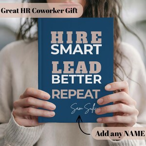 Könnte beinhalten: Ein marineblaues Notizbuch mit den Worten "HIRE SMART LEAD BETTER REPEAT" in weißer und hellbrauner Schrift. Der Text "Add any NAME" steht unter dem Notizbuch. Der Text "Great HR Coworker Gift" steht oben.