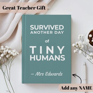 Può includere: Un diario con copertina rigida color verde acqua con testo bianco che recita SURVIVED ANOTHER DAY of TINY HUMANS e - Mrs Edwards. La copertina del libro presenta un layout pulito e centrato con caratteri grassetti sans-serif per il titolo.