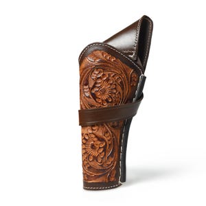 Könnte beinhalten: Ein braunes Lederholster mit aufwendigen floralen Schnitzereien. Das Holster hat einen dunkelbraunen Riemen und Besatz mit weißen Nähten. Das Design ist im klassischen Western-Stil gehalten und eignet sich zum Tragen einer Schusswaffe.