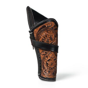 Könnte beinhalten: Eine braune Lederholster mit aufwendiger floraler Prägung. Die Holster hat einen schwarzen Lederriemen und -besatz mit weißen Nähten. Die Oberseite ist aus schwarzem Leder. Das Design ist im klassischen Western-Stil gehalten.