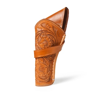 May include: A tan leather holster featuring floral embossing. The holster has a curved design with a strap, intended for a firearm. The leather is a warm, medium brown colour.