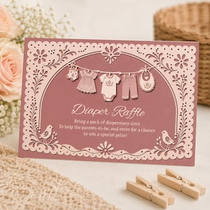 May include: A rectangular dusty rose diaper raffle card featuring a decorative laser-cut style border with flowers and birds. A clothesline displays a sock, dress, onesie, pants, and bib. Text reads: Diaper Raffle, Bring a pack of diapers(any size) To help the parents-to-be, and enter for a chance to win a special prize!