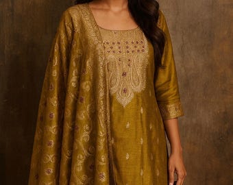 May include: Mustard-colored embroidered tunic and shawl set. The tunic features a square neckline and three-quarter sleeves. The shawl and tunic are adorned with intricate gold embroidery and small maroon accents. The outfit is made of a shiny fabric.