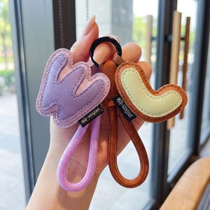 May include: A collection of keychains in various shapes and colors. One keychain is a lavender-colored letter "W" with a pink strap. Another is a brown shape with a light green center and a brown strap. The text "yxxlian-life" is visible on the straps.