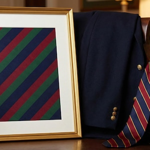 May include: A framed artwork with diagonal stripes in green, red, and navy blue sits on a wooden chair next to a navy blazer. A striped tie with red, navy, and gold stripes hangs over the chair's arm, suggesting a classic, preppy aesthetic.