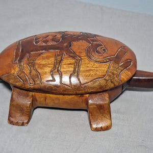 May include: A wooden turtle-shaped box with a hinged lid. The box is carved with an animal design on the lid and has four legs and a tail. The wood has a warm, brown tone.