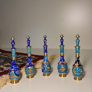 Peut inclure: Cinq flacons décoratifs bleus et dorés avec des motifs floraux complexes. Chaque flacon a une forme élancée et allongée, avec une base et un sommet dorés. Les flacons sont disposés en rangée, mettant en valeur leur artisanat détaillé.