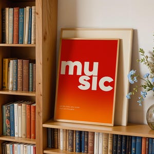 Puede incluir: Un p&oacute;ster enmarcado con la palabra "music" en letras blancas grandes sobre un fondo degradado rojo y naranja. El p&oacute;ster se exhibe en una estanter&iacute;a de madera con una colecci&oacute;n de libros. El texto "Let the music stay louder than your thoughts" est&aacute; en la parte inferior.