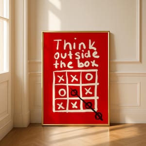 Może przedstawiać: Oprawiony wydruk artystyczny z czerwonym tłem i złotą ramą. Grafika zawiera biały, ręcznie pisany tekst z napisem "Think outside the box" nad grą w kółko i krzyżyk z niedokończoną linią. Grafika jest wyświetlana na drewnianej podłodze.