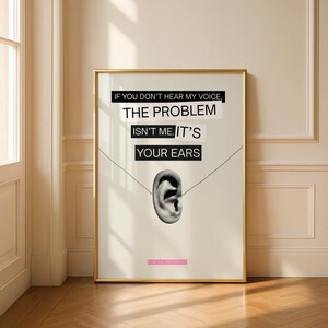 Op de afbeelding: Een ingelijste kunstafdruk met een gouden lijst. De afdruk bevat de tekst "IF YOU DON'T HEAR MY VOICE, THE PROBLEM ISN'T ME. IT'S YOUR EARS" boven een grijswaardenafbeelding van een oor. De onderkant van de afdruk luidt "FUCK THE PATRIARCHY".