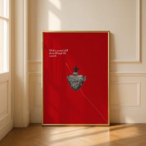 May include: A framed art print with a gold frame, displaying a stylized heart with a crown of thorns and a cross on a red background. The white text reads "What is sacred still shines through the wounds". The artwork evokes a sense of spirituality.