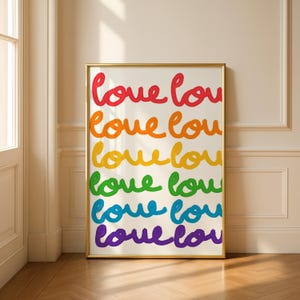 Può includere: Una stampa incorniciata con la parola "amore" ripetuta in un arcobaleno di colori: rosso, arancione, giallo, verde, blu e viola. L'opera d'arte è presentata in una cornice dorata ed è appoggiata a un muro.