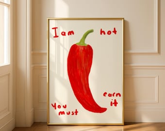 May include: A framed art print showing a red chilli pepper with a green stem on a white background. The words "I am hot, You must earn it" are written in red. The frame is gold.