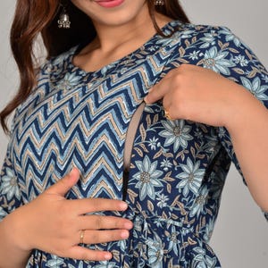 Puede incluir: Vestido de maternidad azul marino con estampado floral y chevron. El vestido presenta un cuello redondo, mangas tres cuartos y cintura fruncida. El vestido tiene una abertura discreta para la lactancia. El vestido está adornado con detalles en azul claro y beige.