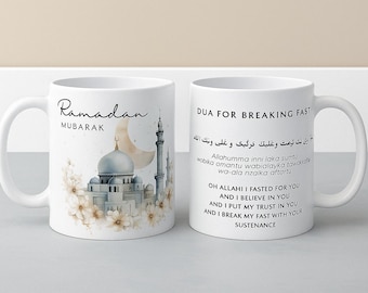 May include: Two white ceramic mugs. One mug features the text "Ramadan Mubarak" with a mosque illustration and a crescent moon. The other mug has text in Arabic and English, "Dua for Breaking Fast."