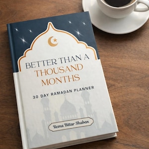 May include: A hardcover planner titled "Better Than a Thousand Months" with a 30-day Ramadan theme. The cover features a gold crescent moon and star design on a navy blue background. A cup of coffee sits nearby.