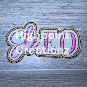 May include: Embroidered patch with the text "She EO" in pink script and block letters, outlined in gold and white. The words "Highpoint Creationz" are also embroidered on the patch.