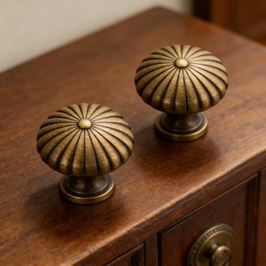 Könnte beinhalten: Zwei antike Messing-Schrankknöpfe mit geripptem, rundem Design. Die Knöpfe sind auf einer dunklen Holzoberfläche montiert und zeigen ihre gealterte, Vintage-Ästhetik. Die Knöpfe haben ein zentrales kreisförmiges Detail.